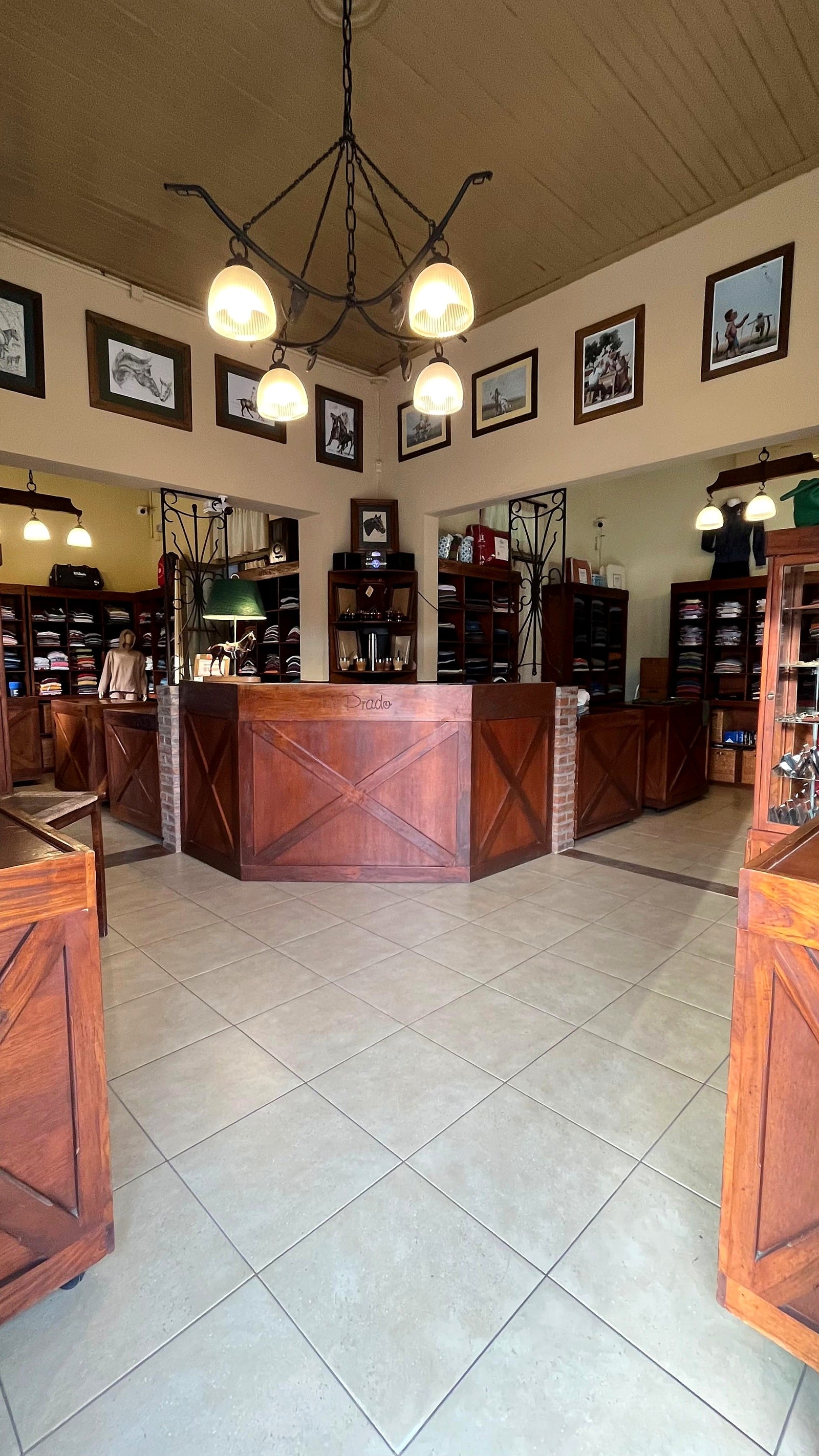 Vista del salón desde la entrada: piso claro, araña de hierro, mostradores de madera y estanterías con ropa.
