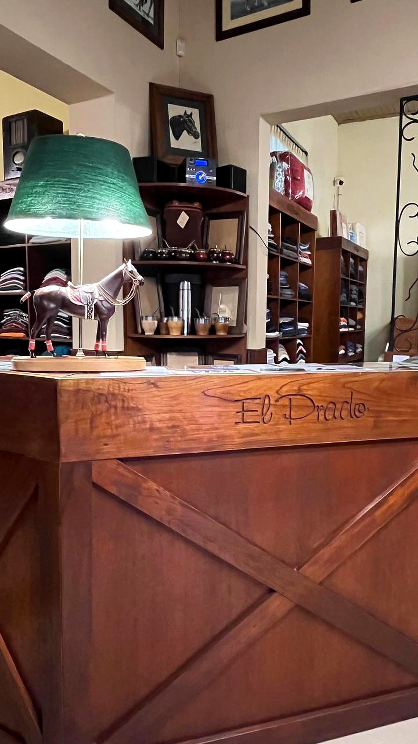 Mostrador con la lámpara del caballo y, detrás, estanterías con mates, termos y ropa.